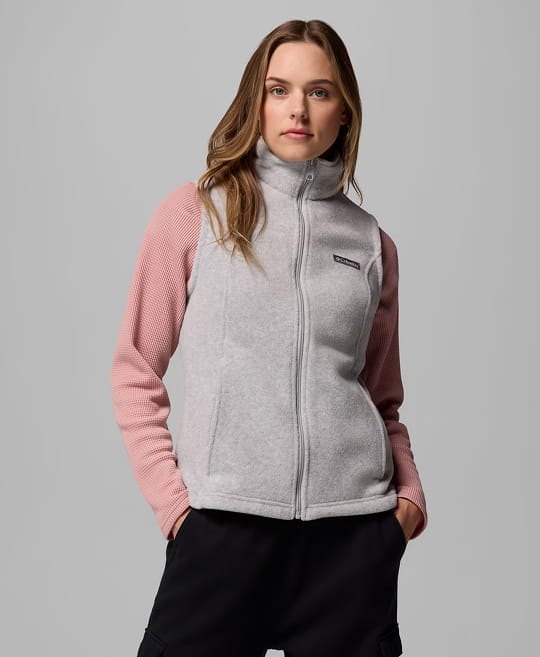 A woman wearing a long sleeve pink shirt and grey vest.
