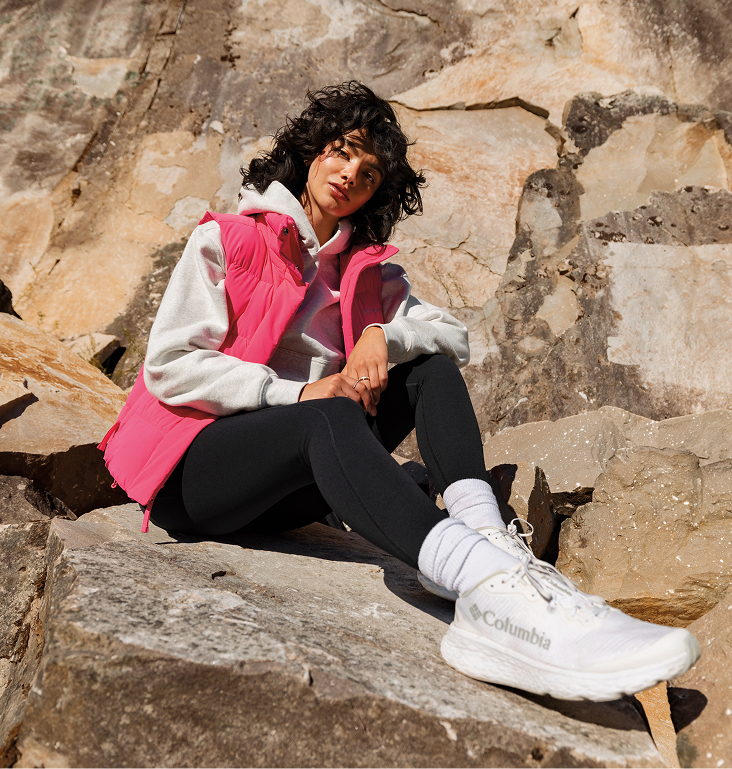A woman sits on a rock wearing a pink Columbia vest. 