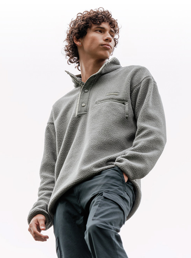 A man wearing a gray fleece pullover against a cloudy sky.