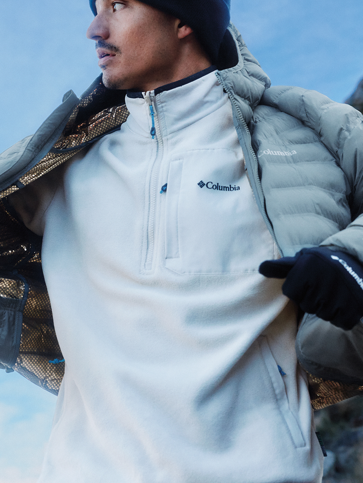 A man taking off his blue puffer to reveal a light blue fleece pullover.