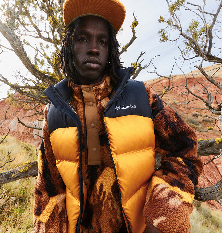 A man wears an orange and black Columbia vest over a dark orange Columbia fleece. 
