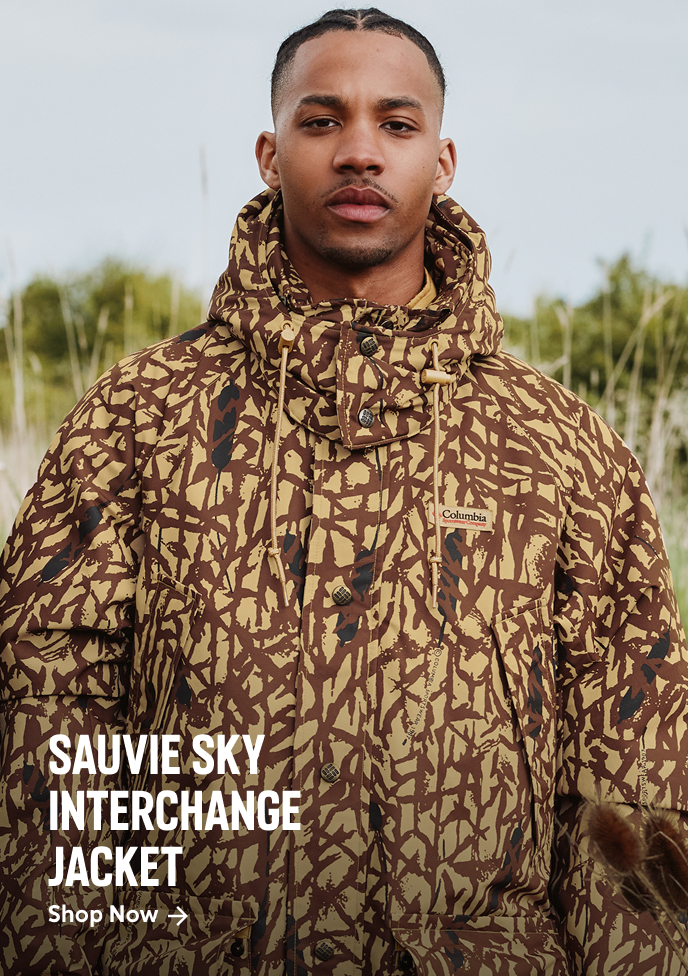 A man standing outside, wearing a camo jacket with text: SAUVIE SKY INTERCHANGE JACKET