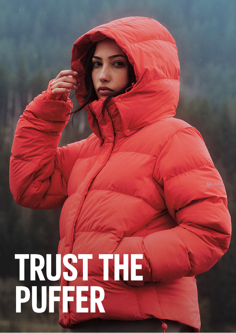 A woman wearing a red puffer jacket outside with text: TRUST THE PUFFER